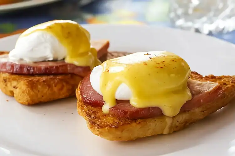 Close-up of Eggs Benedict with ham and hollandaise sauce on toasted bread.